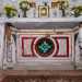 Al centro il grazioso altare in legno, ricco di immaginette sacre e vasetti di fiori, mostra nella base eleganti elementi ricolorati nel tempo con toni rosso, verde e dorato coperti da una bianca tovaglia ricamata